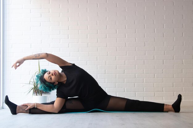 Foto la longitud completa de la mujer sentada en el suelo contra la pared en el deporte doméstico