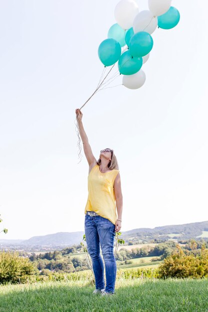 Foto la longitud completa de la mujer sosteniendo globos contra el cielo despejado