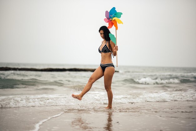 La longitud completa de la mujer sosteniendo un juguete de rueda mientras camina en la playa