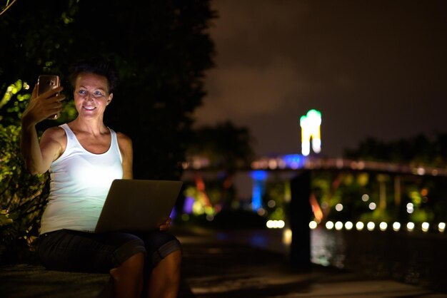 Foto la longitud completa de la mujer usando el teléfono móvil por la noche