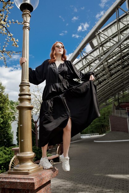 Foto la longitud completa de la mujer en un vestido negro de gran tamaño caminando a ninguna parte contra la estructura construida al aire libre