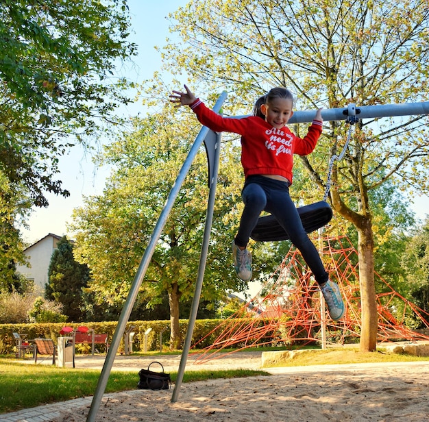 Foto la longitud completa de la niña saltando del columpio en el patio de recreo