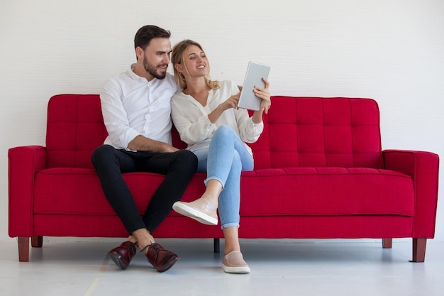 Longitud completa de una pareja joven usando una tableta digital mientras está sentada en el sofá