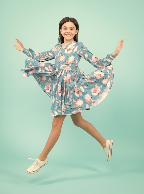 Longitud total alegre adolescente niño salto disfrutar regocijarse ganar aislado sobre fondo azul Niña pequeña en vestido de verano saltando Emocionado adolescente asombrado y alegre emociones