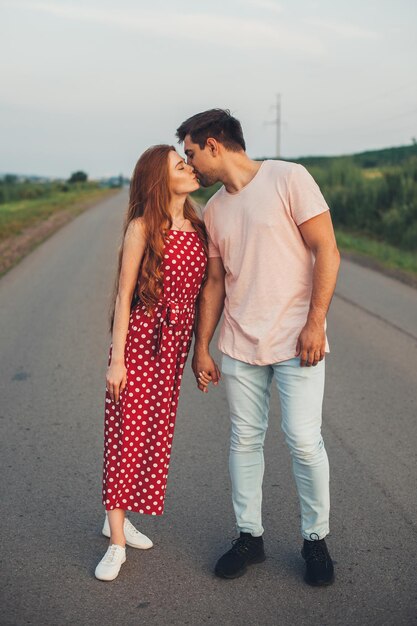 Longitud total de una apasionada pareja caucásica posando mientras se doran las manos y se besan en un camino sobre p...