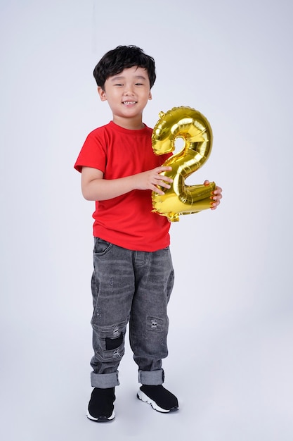 Longitud total del cuerpo de la sonrisa feliz del niño pequeño asiático con el globo del número de la hoja, aislado