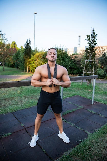 Longitud total de un culturista masculino en un gimnasio al aire libre trabajando sin camisa tiene una expresión de satisfacción y su verano