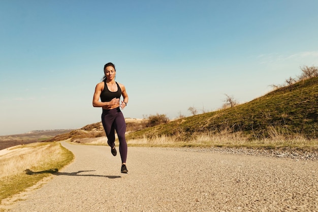 Longitud total de deportista de construcción muscular sonriente corriendo en el espacio de copia de carretera