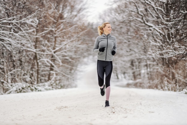 Longitud total de feliz deportista de mediana edad corriendo en la naturaleza en el día de invierno cubierto de nieve. Fitness al aire libre, ejercicios cardiovasculares, ejercicios en la naturaleza.