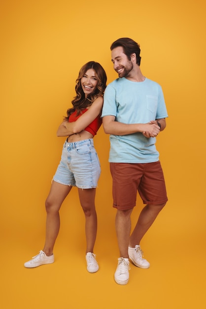 Foto longitud total de la hermosa joven pareja sonriendo mientras está de pie contra el fondo amarillo