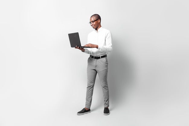 Foto longitud total de hombre de negocios joven negro sosteniendo una computadora portátil sobre fondo gris concepto profesional.