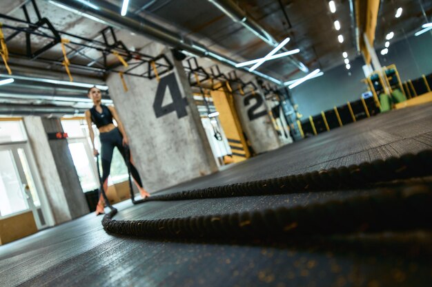 Longitud total de una joven atlética vistiendo ropa deportiva haciendo ejercicio con cuerdas de batalla en