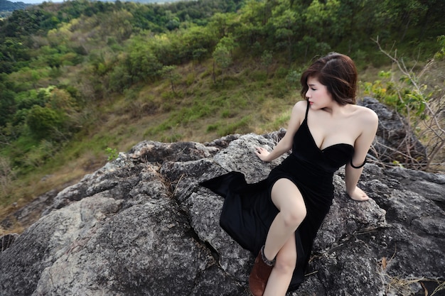 Longitud total joven hermosa mujer asiática, cabello largo en vestido negro sentado en la naturaleza al aire libre