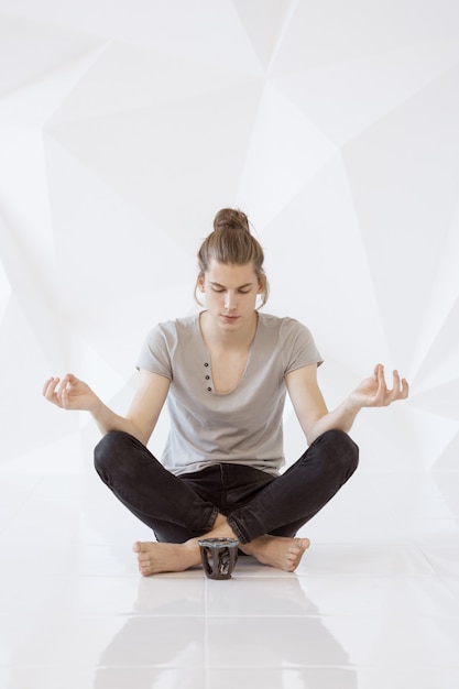 Longitud total de un joven meditando en posición de loto contra el fondo blanco del polígono