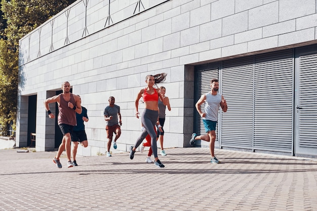 Longitud total de jóvenes en ropa deportiva para correr mientras hacen ejercicio en la acera al aire libre
