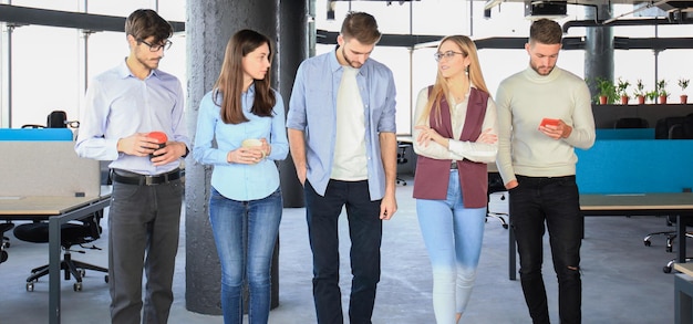 Longitud total de jóvenes con ropa informal elegante discutiendo negocios y sonriendo mientras caminan por la oficina