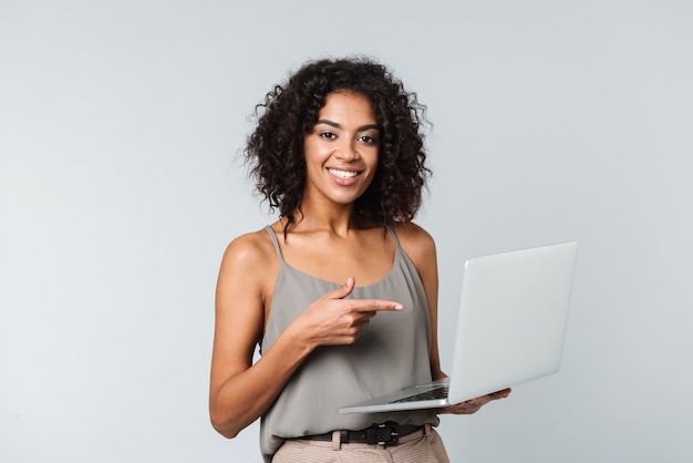 Longitud total de una mujer africana joven feliz vestida casualmente que se encuentran aisladas, trabajando en equipo portátil