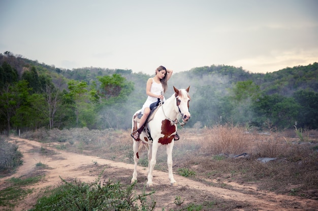 La longitud total de la mujer a caballo en el campo por árboles contra el cielo.