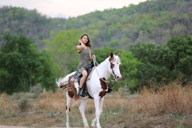 La longitud total de la mujer a caballo en el campo por árboles contra el cielo.