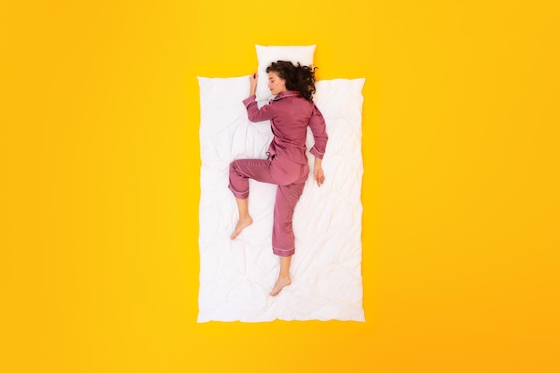 Longitud total de mujer durmiendo la siesta en ropa de dormir cómoda fondo amarillo