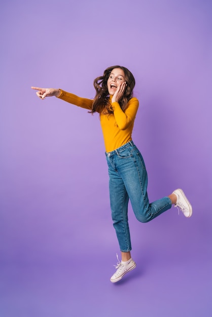 Longitud total de mujer hermosa joven con cabello largo castaño sonriendo y señalando con el dedo en copyspace aislado