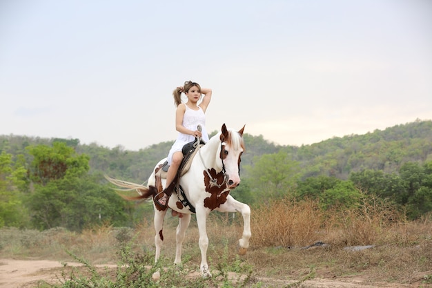 La longitud total de la mujer en el vestido a caballo en el campo por árboles contra el cielo