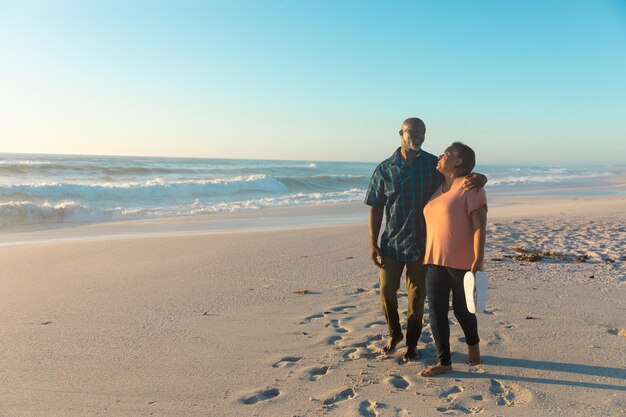 Longitud total de pareja de ancianos afroamericanos caminando en la playa contra el cielo con espacio de copia