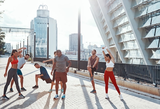 Longitud total de personas en ropa deportiva calentando y estirando mientras hacen ejercicio al aire libre