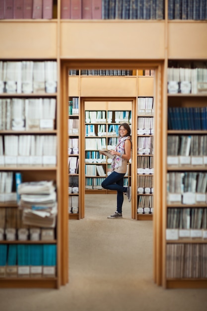 Longitud total de una sonriente estudiante de pie en la biblioteca