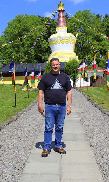 Foto longitude completa de um homem de pé em uma calçada contra uma estrutura construída durante um dia ensolarado