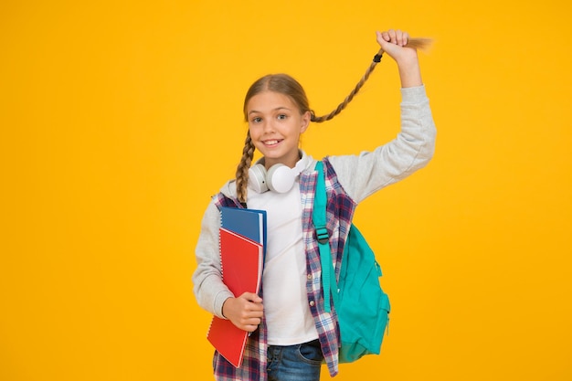 Foto longo e trançado aluno pequeno bonito segura trança de cabelo comprido em fundo amarelo adorável menina usa estilo de cabelo comprido estilizando cabelo comprido para a escola