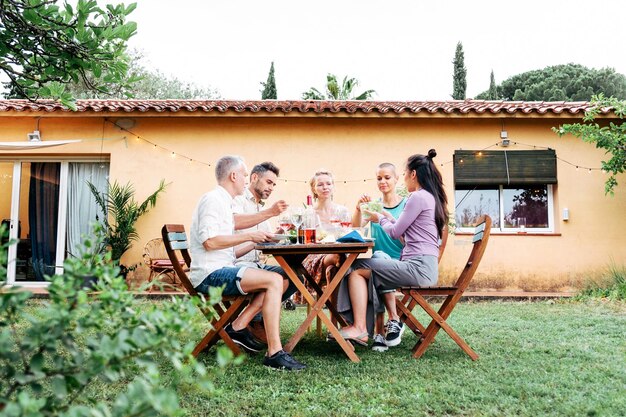 Longview de un grupo de amigos adultos que tienen una cena en el patio trasero de la casa con cerveza y vino