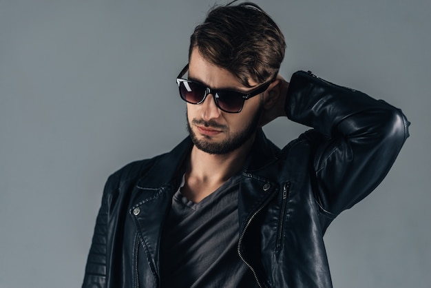 Look moderno. Jovem confiante em óculos de sol, olhando para baixo em pé contra um fundo cinza