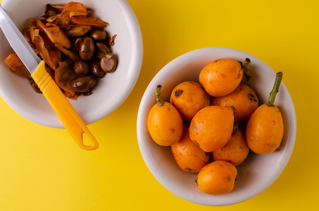 Foto loquats maduros frescos y pelados en un tazón blanco y un cuchillo en amarillo