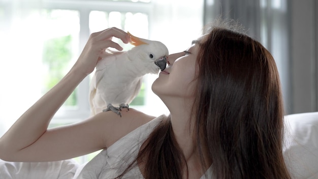 Loro cacatúa sentado en el hombro de la mujer y besándola en la cama por la mañana