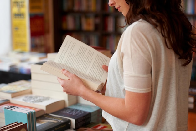 Lost in the pages Eine abgeschnittene Aufnahme einer jungen Frau, die ein Buch liest, während sie in einem Buchladen steht