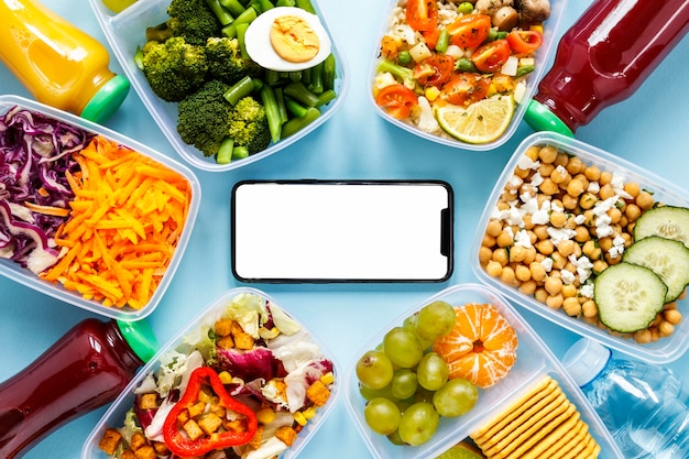 Foto lote de comida cozida em uma variedade de recipientes com smartphone em branco