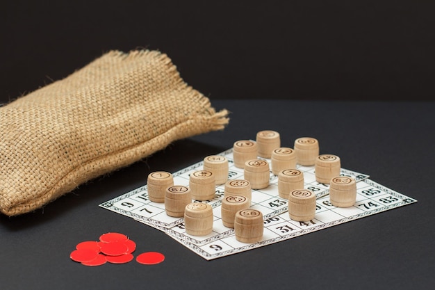 Loto de jogo de tabuleiro Barris de loteria de madeira com cartões de jogo de saco e fichas vermelhas sobre fundo preto