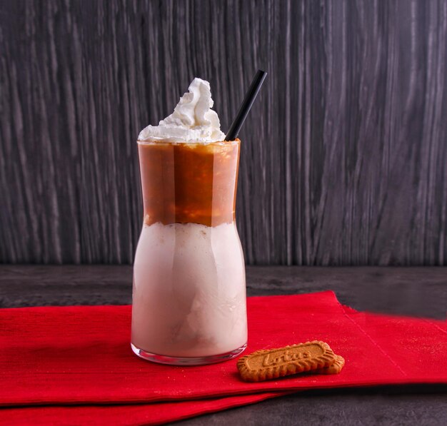 Lotus Tiramisu Milkshake cubierto de crema batida y una salpicadura de polvo de cacao servido en un vaso aislado en el fondo vista lateral de la bebida de postre