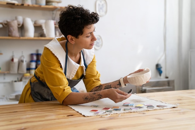 Louças artesanais, fazendo com que a mulher artista escolha a cor da tinta para o copo feito à mão no estúdio para pedidos online