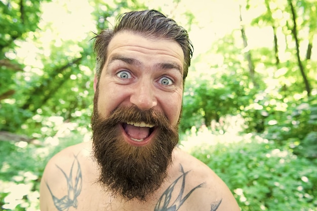 Loucura de verão Homem alegre hipster barbudo tirando selfie na natureza selvagem Homem cara emocional louco sobrevivendo na floresta quente Conceito de férias de verão Se divertindo Blogger ambiente natural de verão