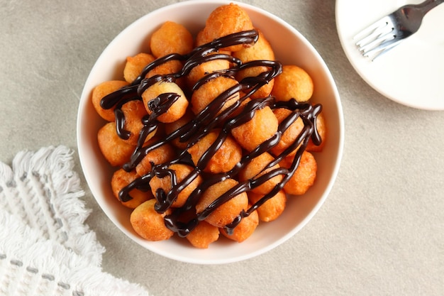 Loukoumades, luqaimat o lokma con cobertura de chocolate en un plato blanco servido con un té.