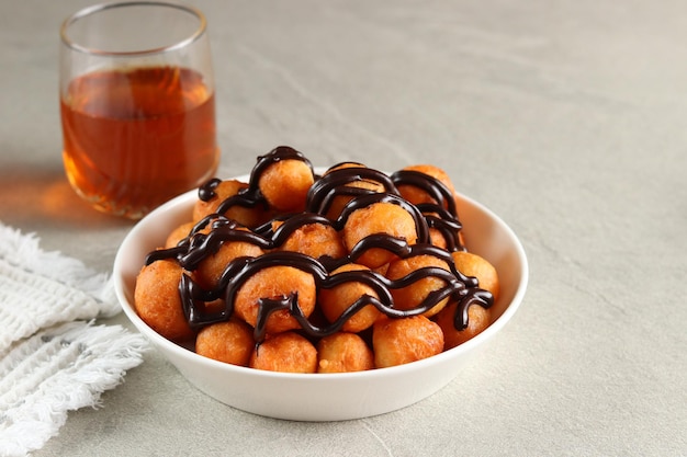 Loukoumades, luqaimat o lokma con cobertura de chocolate en un plato blanco servido con un té