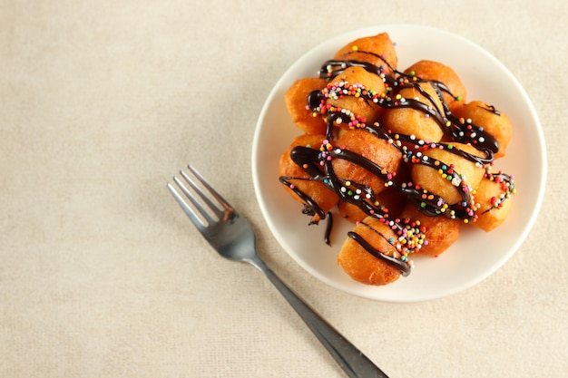 Loukoumades, luqaimat ou lokma com cobertura de chocolate com polvilho colorido em um prato branco