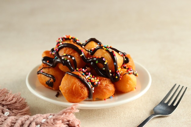 Loukoumades, luqaimat ou lokma com cobertura de chocolate com polvilho colorido em um prato branco