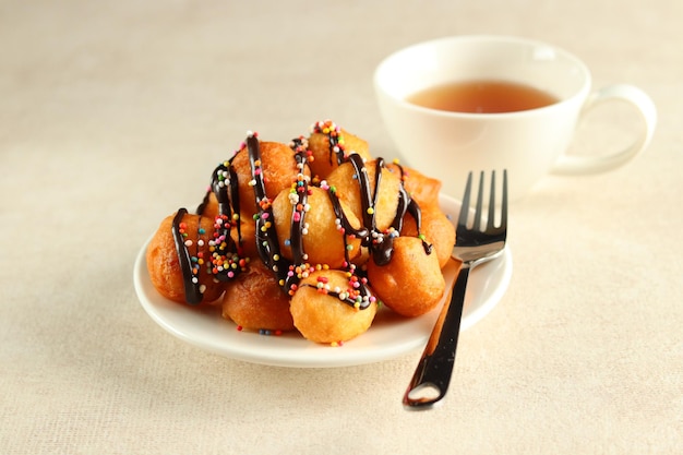 Loukoumades, luqaimat ou lokma com cobertura de chocolate com polvilho colorido em um prato branco