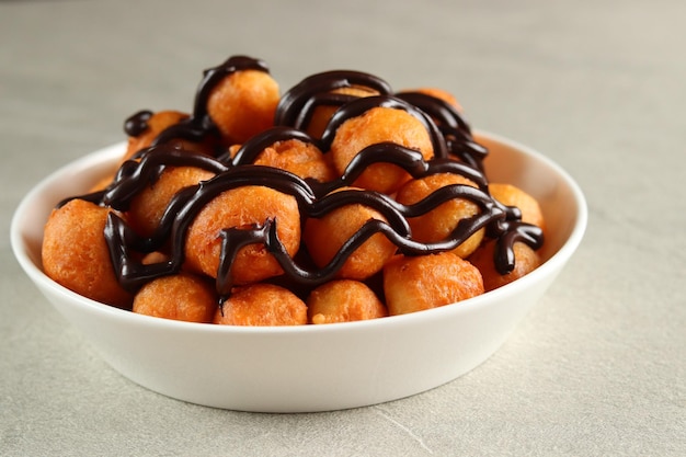 Loukoumades, luqaimat ou lokma com cobertura de chocolate em um prato branco servido com chá