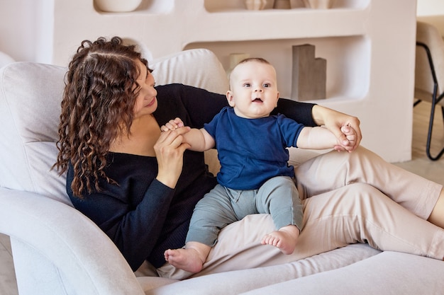 Lounge com a jovem mãe e o bebê que se sentam no sofá