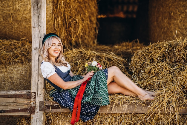 Foto lourinha em vestidos casuais dirndl, tradicional com buquê de flores do campo, sentado na cerca de madeira na fazenda