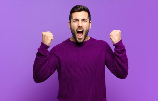 Louro adulto bonito gritando agressivamente com uma expressão de raiva ou com os punhos cerrados celebrando o sucesso